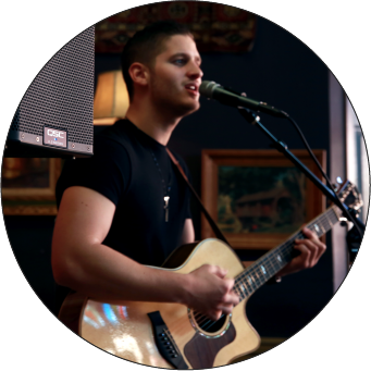 Image of man with an acoustic guitar singing into a microphone