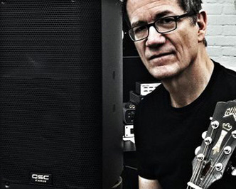 Jon Herington next to a QSC Loudspeaker