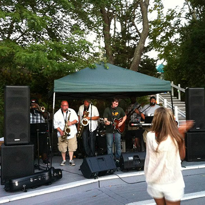 A band performing on a small stage surrounded by QSC Speakers