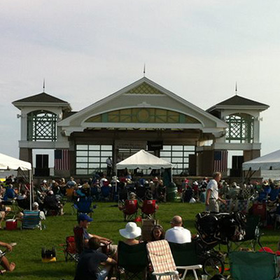  A crown seated in a grass field facing a stage with QSC speakers